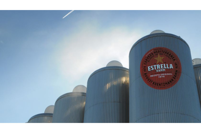 Große Silos der Estrella Damm Brauerei unter einem blauen Himmel mit Kondensstreifen.